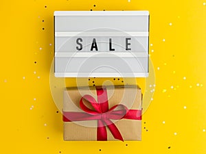 Brown gift boxes with red ribbon and Light board with text Sale. Yellow background with multicolored confetti. Flat lay style.