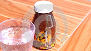 Brown glass bottle with colorful capsules, pills, tablets of medicine and vitamin take with water, isolated in wooden background,