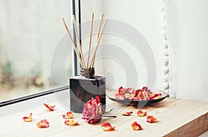 Brown glass bottle container with wood stick diffusers on home wooden window sill with beautiful dry pink rose petals for decorati photo
