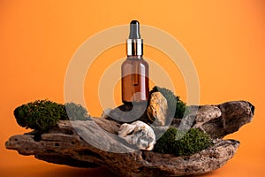 Brown glass bottle with cosmetic product mock up on a wooden stand with moss orange background. Natural cosmetics ingredients