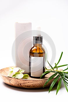 Brown glass cosmetic bottle mock-up with blank white label and green leaves, serum packaging