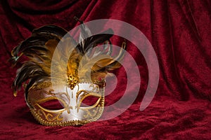 Brown golden venetian carnival mask on a draped red velvet theater curtain