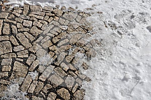 Brown granite paving of irregular stones. Frozen partially snow covered country road courtyard at the entrance to the building. Re