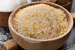 Brown granulated sugar in wooden bowl on black table, closeup