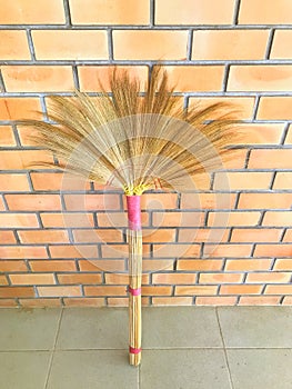 Brown grass broom leaned against the brick wall