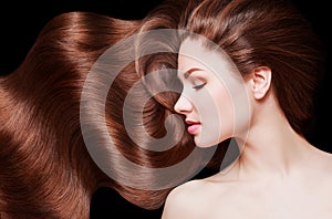 Brown Hair. Beautiful young woman with healthy luxurious long hair on dark background. Hairstyle. Hair cosmetics