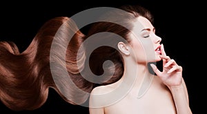 Brown Hair. Beautiful young woman with healthy luxurious long hair on dark background. Hairstyle. Hair cosmetics