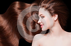 Brown Hair. Beautiful young woman with healthy luxurious long hair on dark background. Hairstyle. Hair cosmetics