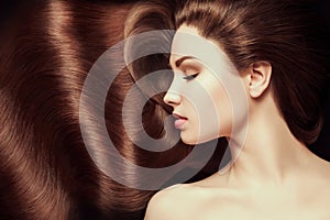 Brown Hair. Beautiful young woman with healthy luxurious long hair on dark background. Hairstyle. Hair cosmetics. Toning