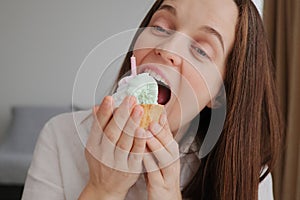 Brown haired beautiful woman biting appetizing piece of cake with cream has sweet tooth feeling temptation to eat delicious