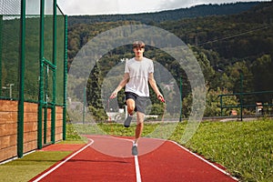 Brown-haired boy with an athletic figure wearing a white T-shirt and black shorts is jumping rope on an athletic oval. Training to