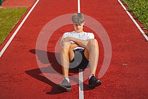 Brown-haired boy with an athletic physique on an athletic oval massages his muscles with a foam roller for better recovery. Post-