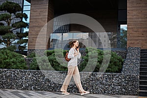 Brown haired business woman talking on mobile phone outdoors, professional woman in stylish attire walking on city street using