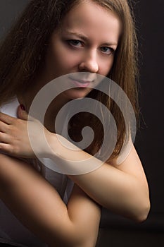 Brown-haired girl on a black background in white blouse. Contemptuous look. Hands at the collar