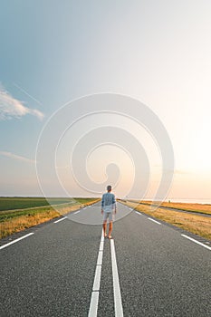 Brown-haired man in a checked shirt walks along a road at sunset on the outskirts of Almere, Netherlands. Fashion lifestyle