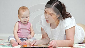 Brown-haired mother reads book to amused baby girl on floor