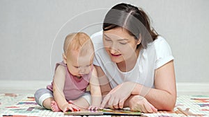 Brown-haired mother reads book to amused baby girl on floor