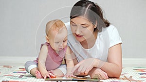 Brown-haired mother reads book to amused baby girl on floor