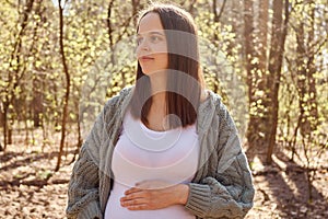 Brown haired pregnant woman enjoying peaceful moments in park embracing nature's serenity and finding comfort during