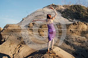 Brown-haired woman in purple glittering dress dancing on sand