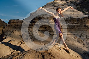 Brown-haired woman in purple glittering dress dancing on sand