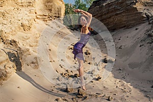 Brown-haired woman in purple glittering dress dancing on sand