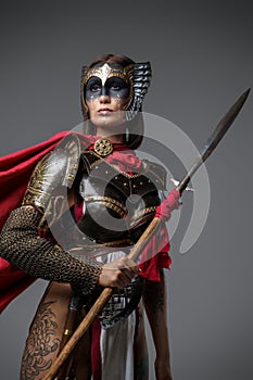 Brown haired woman wielding spear against grey background