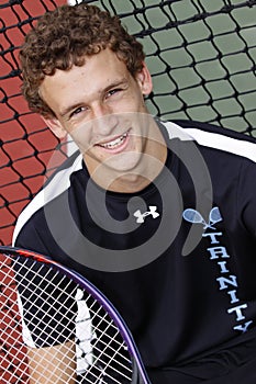 Brown haired young man smiling with tennis racket