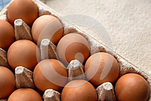 Brown hen eggs in a box made of recycled cardboard are located on a grey wooden countertop in the kitchen. Top view