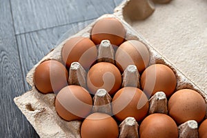 Brown hen eggs lie in a row in a box made of recycled cardboard are located on a grey wooden surface. Healthy farm food