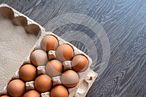 Brown hen eggs lie in a rows in the box made of recycled cardboard. Box is located on a brown wooden countertop in the kitchen.