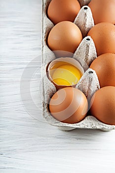 Brown hen`s eggs one egg yolk visible decorated in a box photo