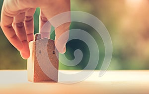 Brown home model made from clay on wooden surface, holding by left hand, blurred green bokeh as background, copy space on right