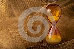 Brown hourglass glass clock on gold honeycomb lattice background. Concept of transience of expiring time is value