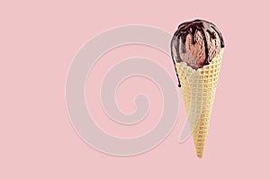 Brown ice cream in crisp waffle cone with chocolate sauce on pastel pink background, mock up for design.