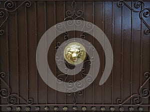 A brown iron fence with a wrought pattern and a golden lion head in the center. Full screen photo