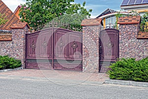 A brown iron gate and a wrought iron door and part of a stone fence