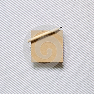 Brown kraft memo pad, empty paper with wooden pencil on gray stripe pattern fabric background