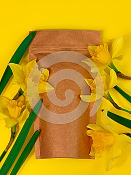 Brown kraft paper pouch bag mockup coffee beans and yellow daffodil flowers on pastel background top view