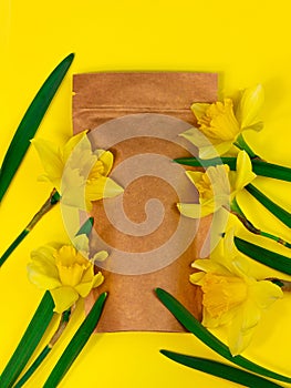 Brown kraft paper pouch bag mockup coffee beans and yellow daffodil flowers on pastel background top view