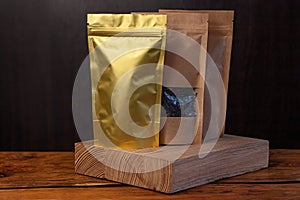 Brown kraft paper pouch bags with coffee beans and tea leaves in wicker basket with white textile on wooden background