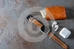 Brown leather accessories. Smart watch, wallet with banknote and headphones.