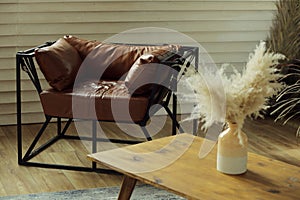 A brown leather armchair in a room with a table and a vase of dry grass