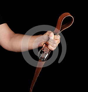 brown leather belt with an iron buckle in a man's hand, black background