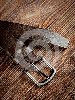 Brown leather belt on a wooden brown background. Close-up
