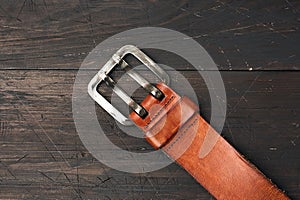 Brown leather men`s belt with metal buckle on a wooden background