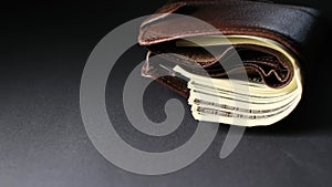 Brown leather men's wallet with cash in dollars on a black background.