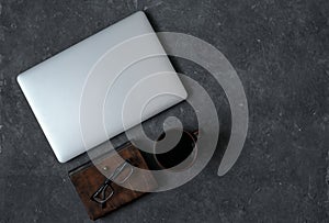 Brown leather notebook, pen, laptop and glasses on gray background