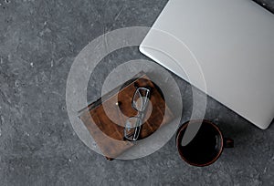 Brown leather notebook, pen, laptop and glasses on gray background