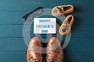 Brown leather shoes, children`s shoes, inscription happy fathers day, and glasses on wooden background